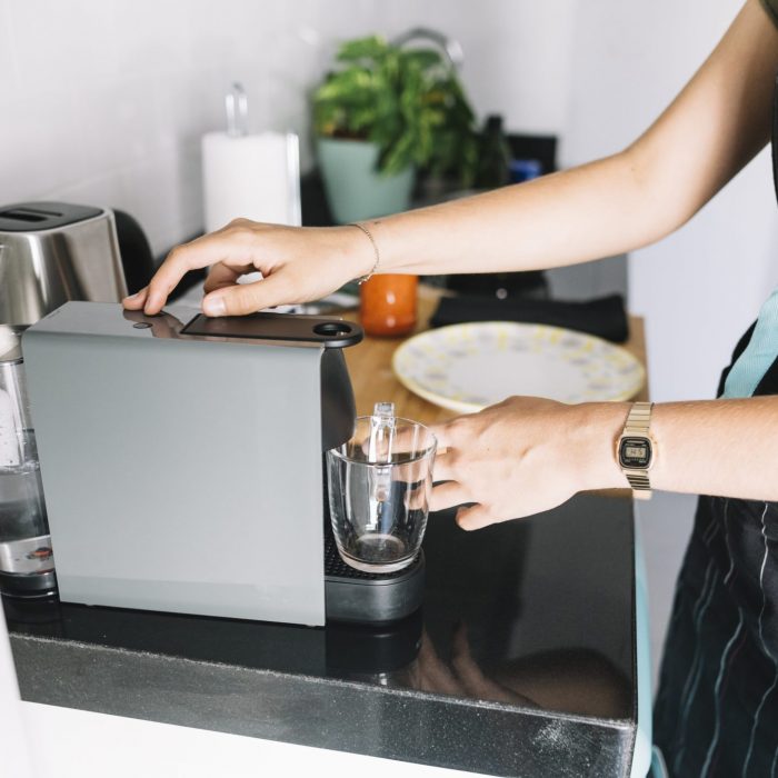 woman-holding-glass-mug-coffee-machine-kitchen-min